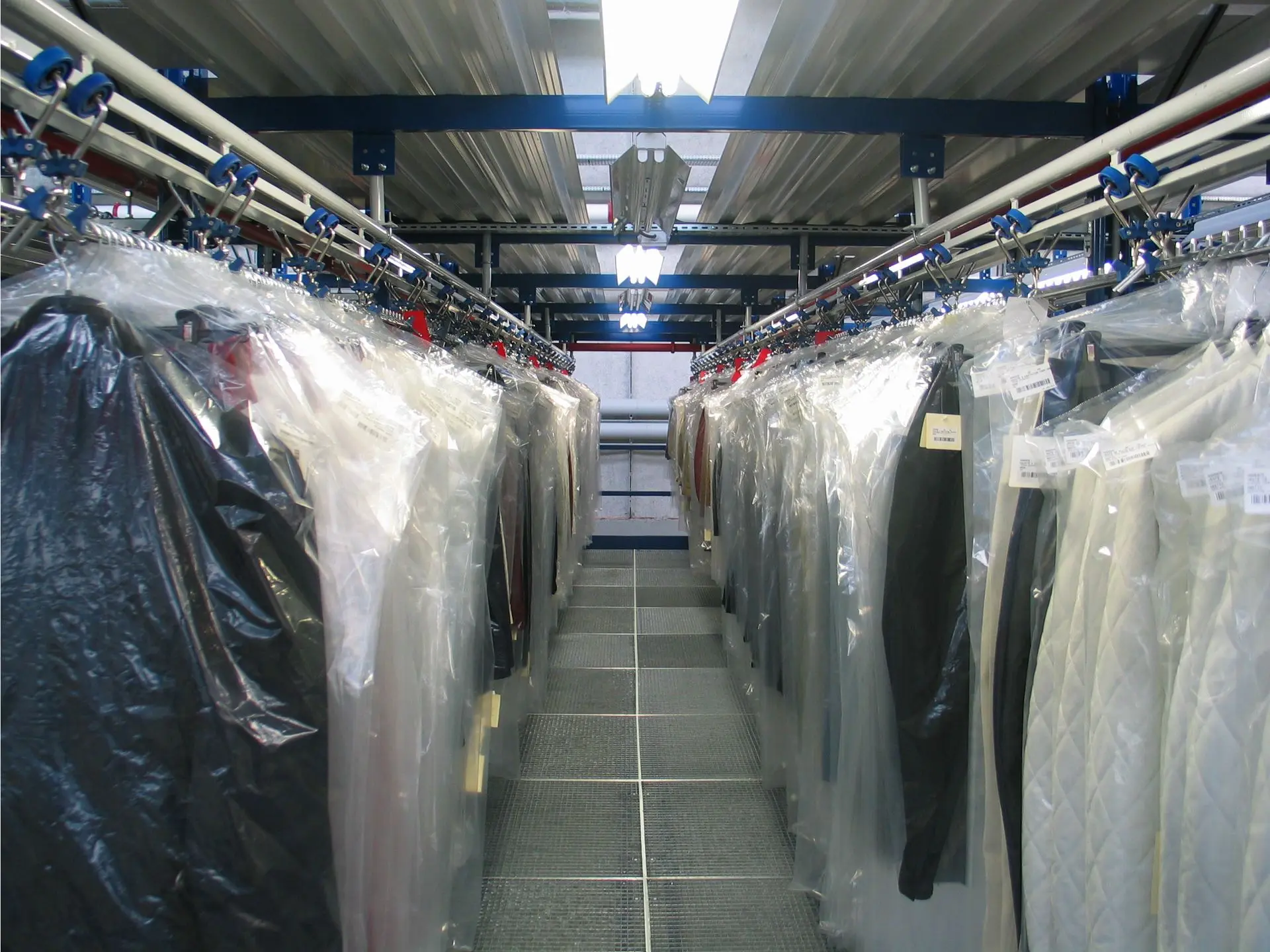 Stockage aérien de vêtements sur cintres avec convoyeur à trolleys en blanchisserie industrielle